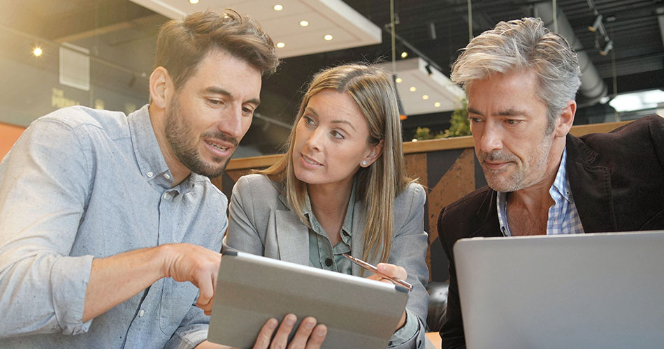 Drei Geschäftsmänner- und frauen schauen auf ein Tablet und sprechen miteinander